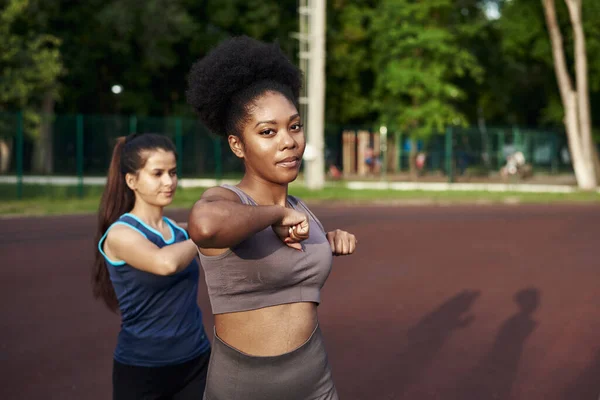 Twee fitte glimlachende jonge vrouw samen trainen in een park doen stretching oefening en hand extensies om soepelheid te verbeteren — Stockfoto