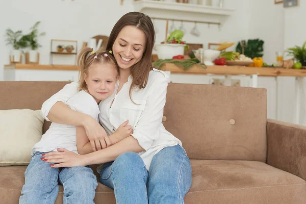 The little girl complains to her mother and cries. A young woman calms her daughter on the couch at home — Stock Photo, Image