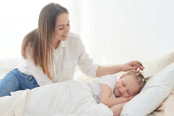 Beautiful young mom wakes up her preteen little daughter in the morning. Tenderness and care. Mothers love — Stock Photo, Image