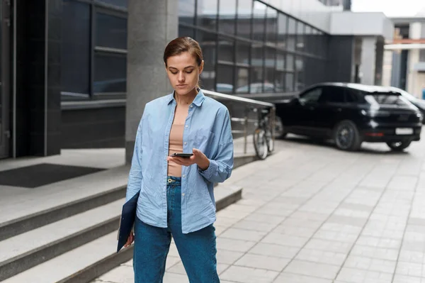 Successful young businesswoman checks email on smartphone during a lunch break outside office. City businesswoman working