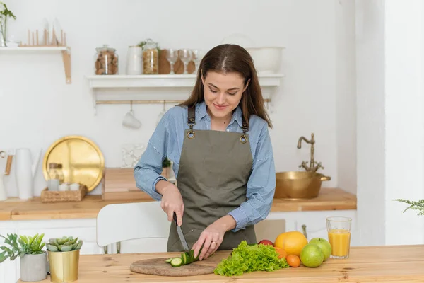 Dieta verde, uma mulher cortou pepinos. Mulher bonita que prepara a salada vegetal saborosa na cozinha em casa — Fotografia de Stock