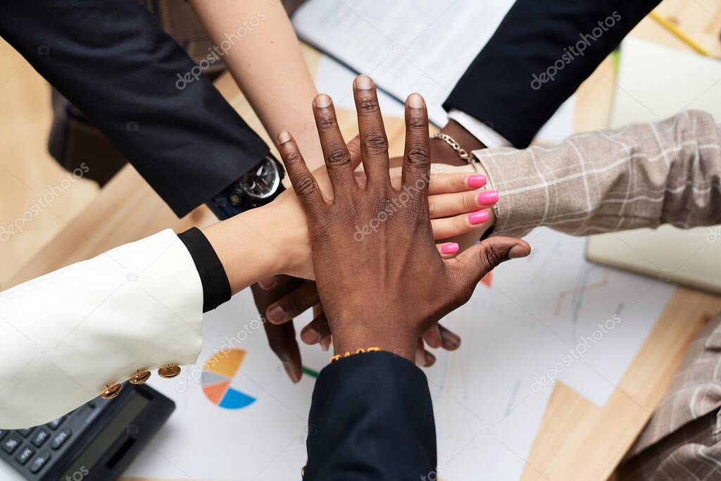 The black leaders hand covers the hands of the business team. A circle from the hands of multiethnic people working together in the office. Leadership and team concept