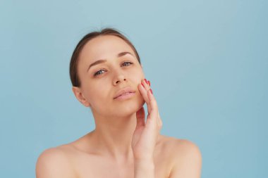 Mavi arka planda temiz ve sağlıklı bir cilde sahip bir kadının güzel portresi. Gülümseyen rüya gibi güzel kadın