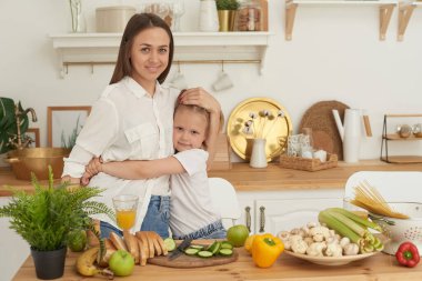 Neşeli anne ve küçük kız mutfakta birlikte salata hazırlıyor ve eğleniyorlar. Kız annesini evde öpüyor.