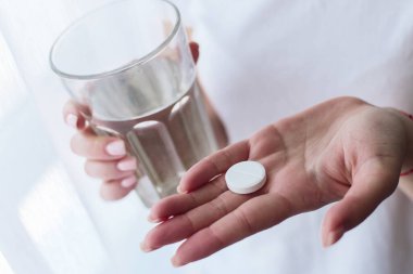 Eller bir bardak su ve ağrı kesici tutar. Sağlık sigortası, tıbbi destek konsepti. Ağrı kesicili kadına yaklaşın.