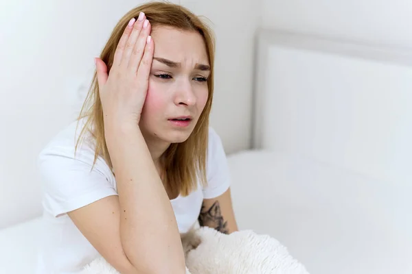 Mujer joven sentada en una cama, sosteniendo la cabeza, teniendo un fuerte dolor de cabeza — Foto de Stock
