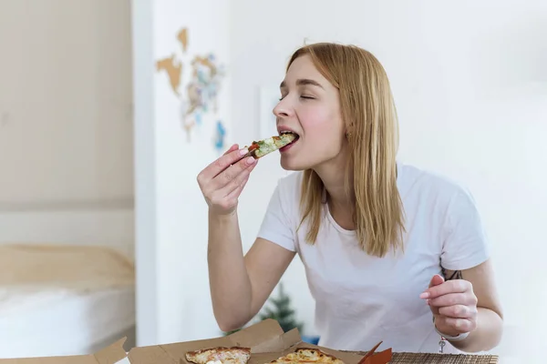 행복 한 젊은 여자 가 집에서 뜨거운 피자 한 조각을 먹고 맛있는 식사를 즐긴다 — 스톡 사진