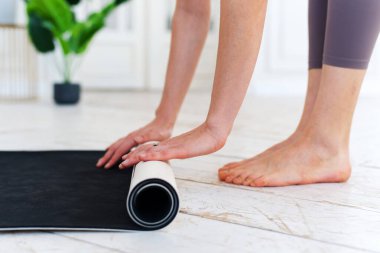 Evde ya da spor salonunda egzersiz yaptıktan sonra gri yoga ya da spor paspası katlayan genç kadınların yakın çekimi. Yoga, spor, sağlıklı yaşam tarzı konsepti