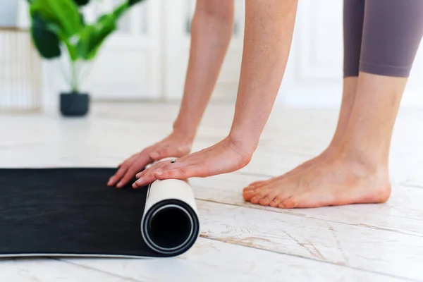 Gros plan des mains de jeunes femmes pliant yoga gris ou tapis de fitness après l'exercice à la maison ou à la salle de gym. Yoga, sport, mode de vie sain concept — Photo