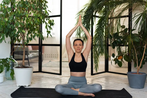 Young woman meditating indoors. pose Young woman smiling for the camera, sitting in the lotus position. Relaxation and meditation at home among the plants — Stock Photo, Image