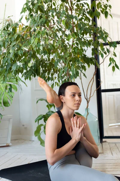 Young beautiful woman is engaged in stretching in a room with plants — Stock Photo, Image