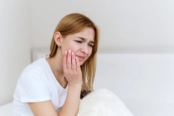 Close-up de uma jovem que sofre de dor de dente enquanto está sentada na cama. Foto de perto de um homem tocando sua bochecha e torcendo os lábios devido à dor de dente — Fotografia de Stock