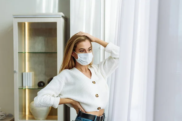 Mujer triste sola durante la pandemia de coronavirus usando mascarilla en el interior de casa para el distanciamiento social. Concepto de crisis de salud mental — Foto de Stock