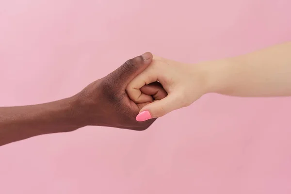 Белая женщина и афроамериканец держатся за руки на розовом фоне. Концепция расизма — стоковое фото