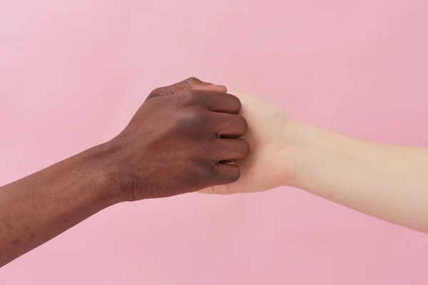 Un apretón de manos entre un hombre afroamericano y una mujer caucásica posando sobre un fondo rosa, saludándose, demostrando relaciones internacionales. Primer plano de tiro. apretón de manos —  Fotos de Stock