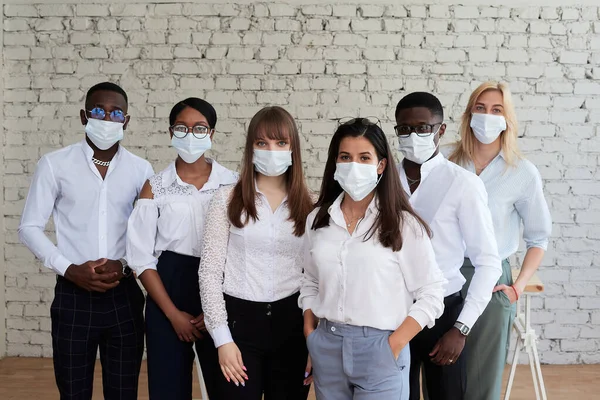 Międzynarodowi pracownicy biurowi stoją w maskach ochronnych i patrzą w kamerę — Zdjęcie stockowe