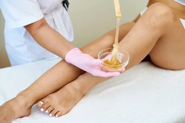 Pracownik salonu kosmetycznego nakłada pastę cukrową do usuwania włosów z miski na nogę klienta — Zdjęcie stockowe