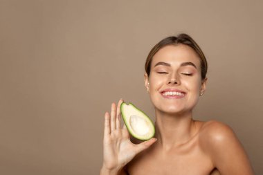 Elinde bej bir arka planda avokado tutan mutlu, genç bir kadın. Doğal güzellik konsepti