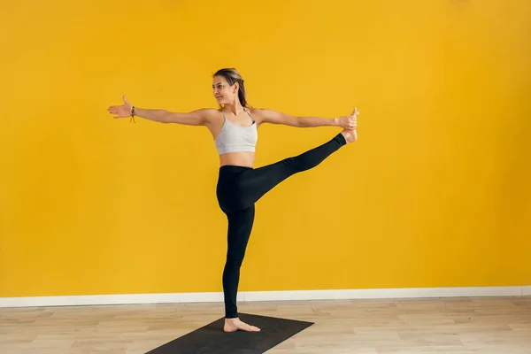 Vacker ung kvinna som utövar yoga inomhus. Utthita Hasta Padangusthasana, Extended Hand to Big Toe pose. Gul bakgrund — Stockfoto