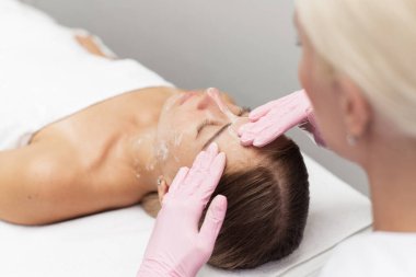 Young beautician or dermatologist doing manual facial cleansing for a woman in a beauty salon. Spa facial massage. Beautiful woman receiving facial massage in a beauty salon. The beautician makes