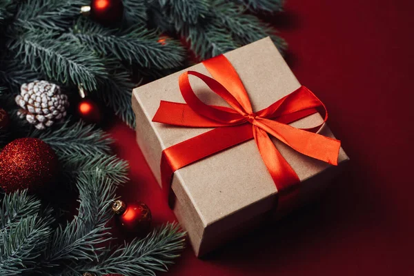 Vánoční koncept. Vánoční dárková krabice s červeným míčkem a větvemi s borovicovými šiškami na červeném pozadí — Stock fotografie
