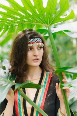 Bitkilerin ve palmiye yapraklarının arka planında Ürdün 'den gelen kız. Arap devletinin ulusal kostümlü Ürdünlü kızı.