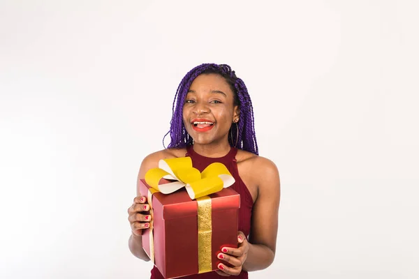 Egy fekete nő egy hatalmas piros ajándékot tart egy arany masnival a kezében, a kamerába néz és mosolyog. Az ünnep koncepciója, újév és karácsony — Stock Fotó