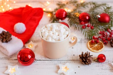 Noel arkaplanı, kahve fincanı ve şekerlemeler, kırmızı Noel oyuncakları, parlayan ışıklar. Mutlu Noeller tebrik kartı.