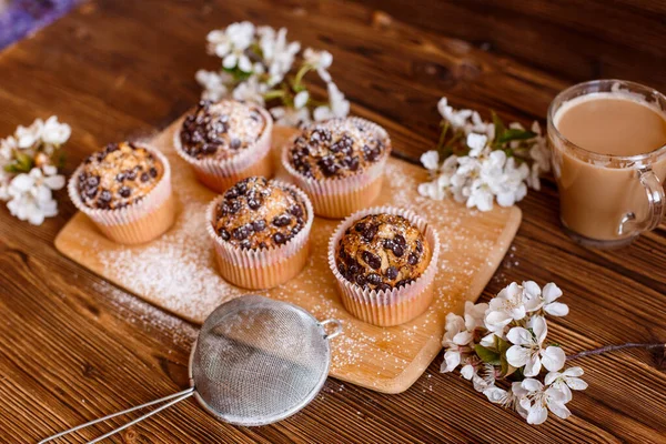 muffins with chocolate chips and a Cup of coffee on a wooden background with a blooming twig