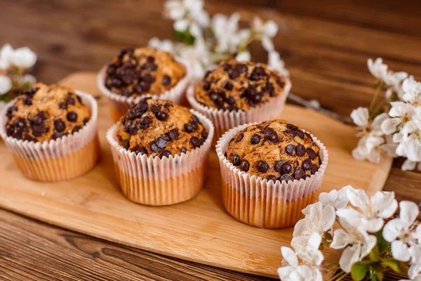 muffins with chocolate chips and a Cup of coffee on a wooden background with a blooming twig