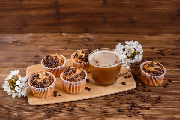 muffins with chocolate chips and a Cup of coffee on a wooden background with a blooming twig
