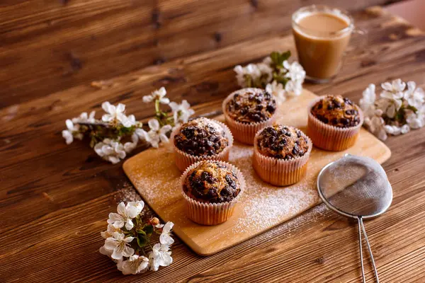 muffins with chocolate chips and a Cup of coffee on a wooden background with a blooming twig