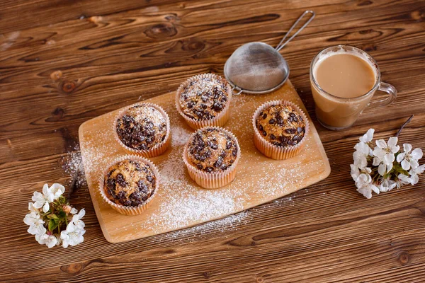 muffins with chocolate chips and a Cup of coffee on a wooden background with a blooming twig