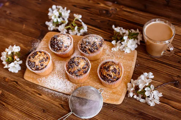 muffins with chocolate chips and a Cup of coffee on a wooden background with a blooming twig