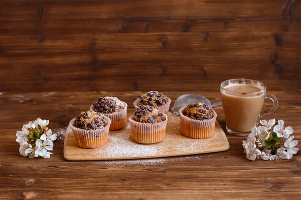 muffins with chocolate chips and a Cup of coffee on a wooden background with a blooming twig