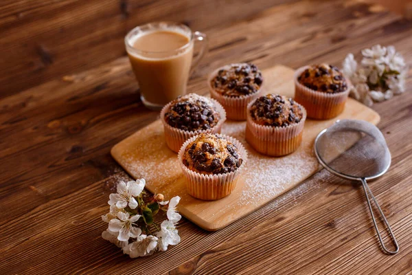 muffins with chocolate chips and a Cup of coffee on a wooden background with a blooming twig