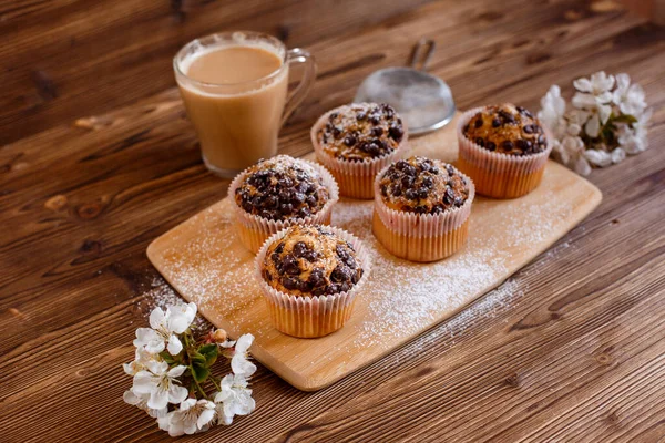 muffins with chocolate chips and a Cup of coffee on a wooden background with a blooming twig