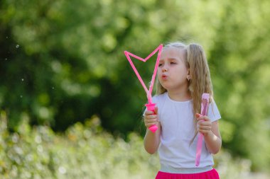 Bir kız yazın parkta sabun köpüğü üflüyor.