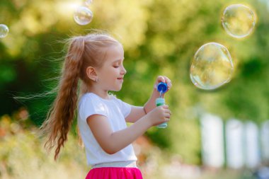 Bir kız yazın parkta sabun köpüğü üflüyor.