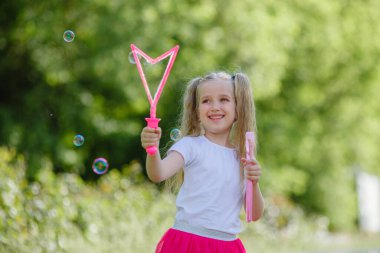 Bir kız yazın parkta sabun köpüğü üflüyor.