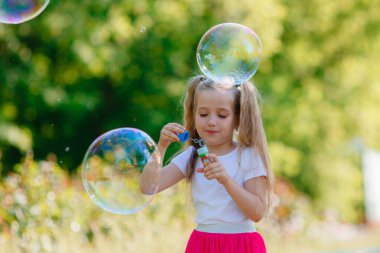 Bir kız yazın parkta sabun köpüğü üflüyor.