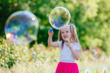 Bir kız yazın parkta sabun köpüğü üflüyor.
