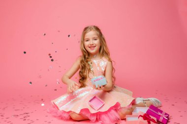 Elinde hediye tutan küçük bir kız pembe bir arka planda gülümsüyor.. 