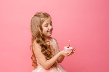 Küçük şirin kız pembe arka planda doğum günü pastasıyla poz veriyor.