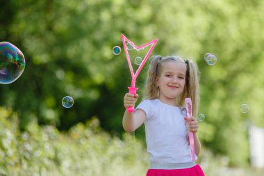 Bir kız yazın parkta sabun köpüğü üflüyor.