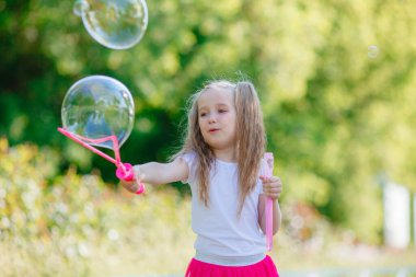 Bir kız yazın parkta sabun köpüğü üflüyor.