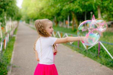 Bir kız yazın parkta sabun köpüğü üflüyor.