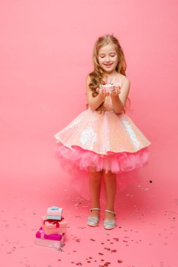 Küçük şirin kız pembe arka planda doğum günü pastasıyla poz veriyor.