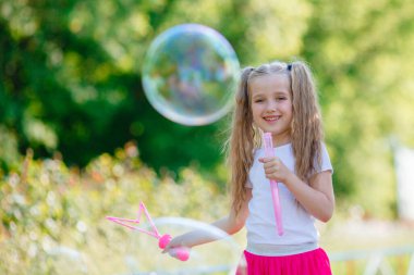 Bir kız yazın parkta sabun köpüğü üflüyor.