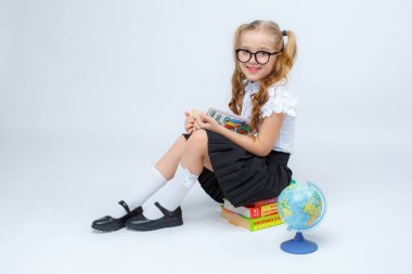 Okul üniformalı ve gözlüklü küçük kız stüdyoda poz veriyor.